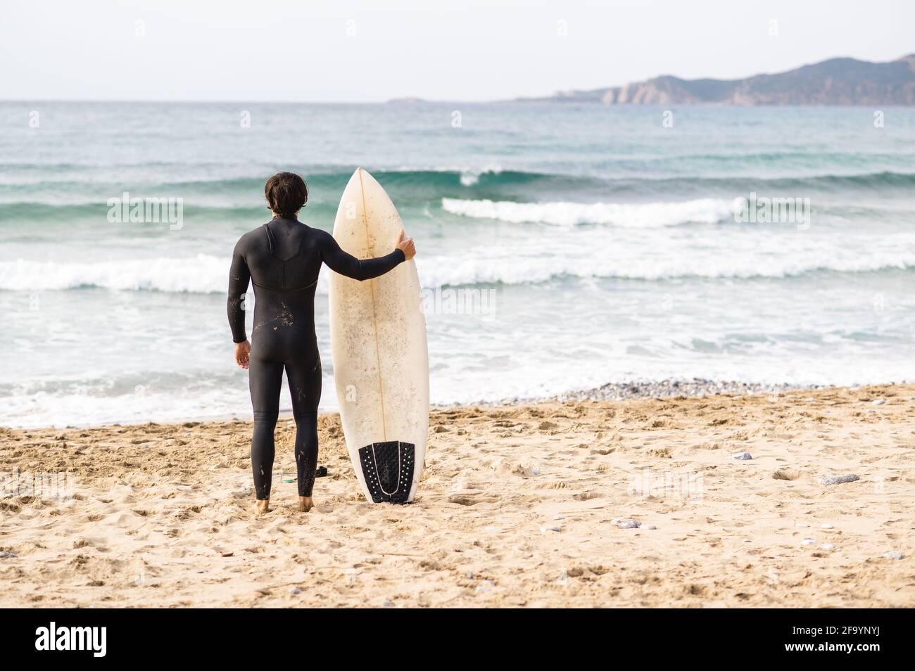 Back view of surfer man wearing diving suit leaning on the surfboard