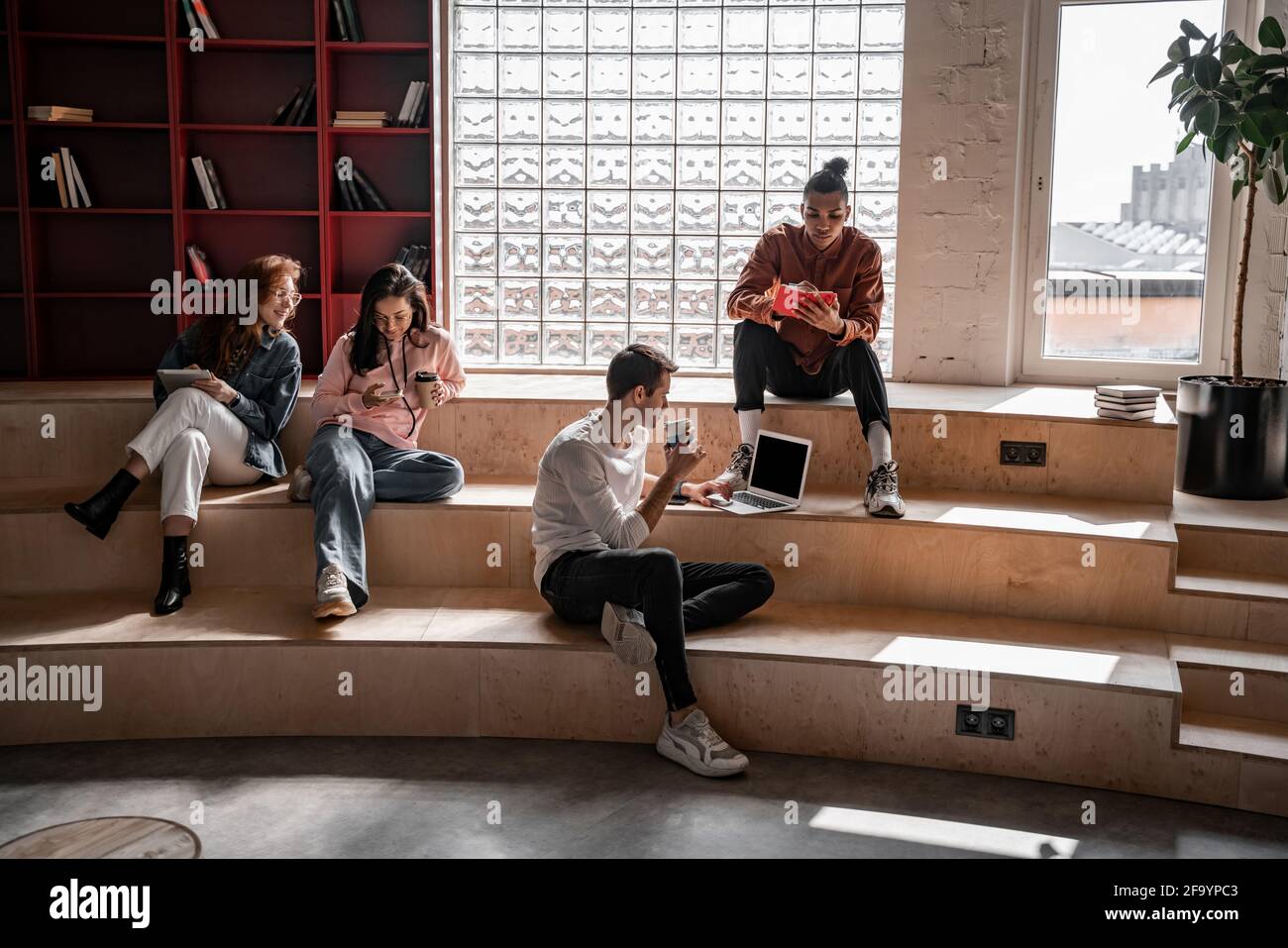 interracial students sitting on stairs and using gadgets Stock Photo