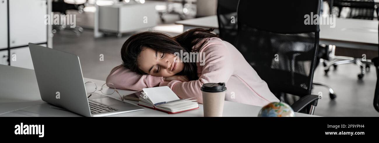 tired student sleeping on desk near laptop and paper cup, banner Stock Photo