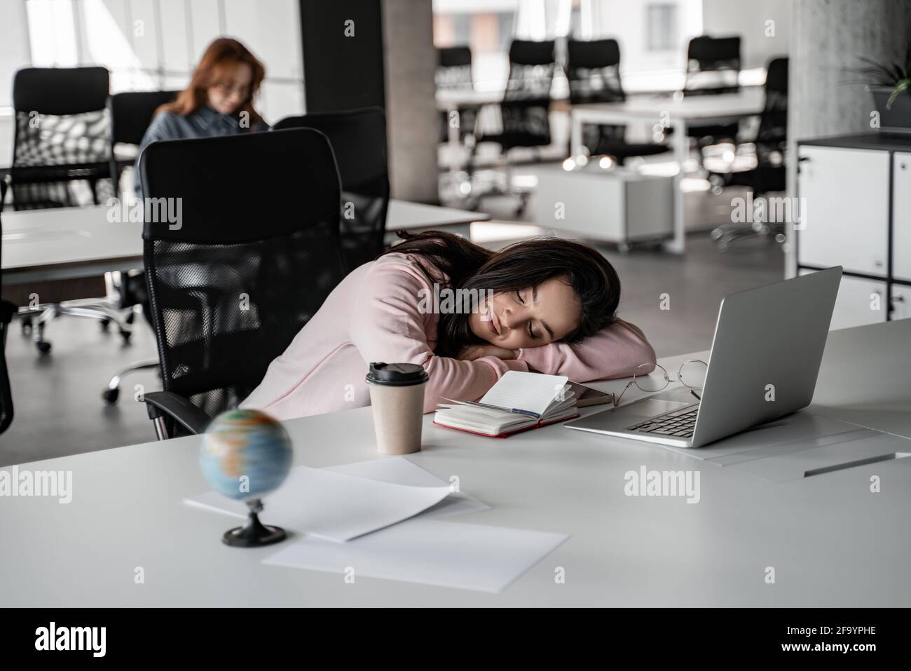 tired student sleeping on desk near laptop and paper cup Stock Photo