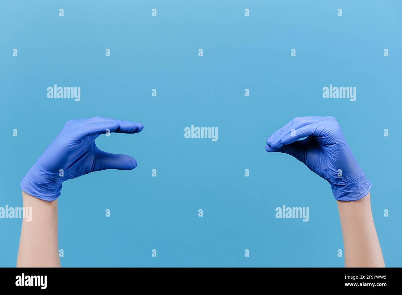 Close up of male showing talking to each other hands, wears medical protective latex gloves, isolated on blue studio background wall with copy space Stock Photo