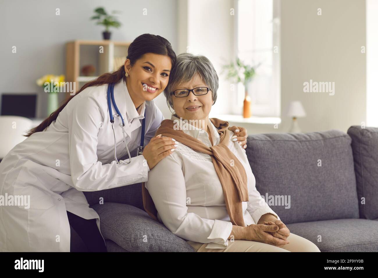 Portrait of smiling young doctor or home care nurse embracing her senior patient Stock Photo