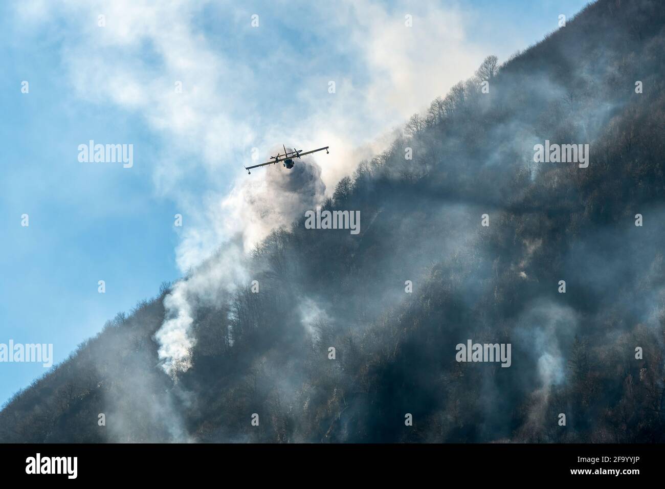 Firefighting Aircraft dropping the water for fighting a fire on mountain above Lake Ghirla in Valganna, province of Varese, Italy Stock Photo