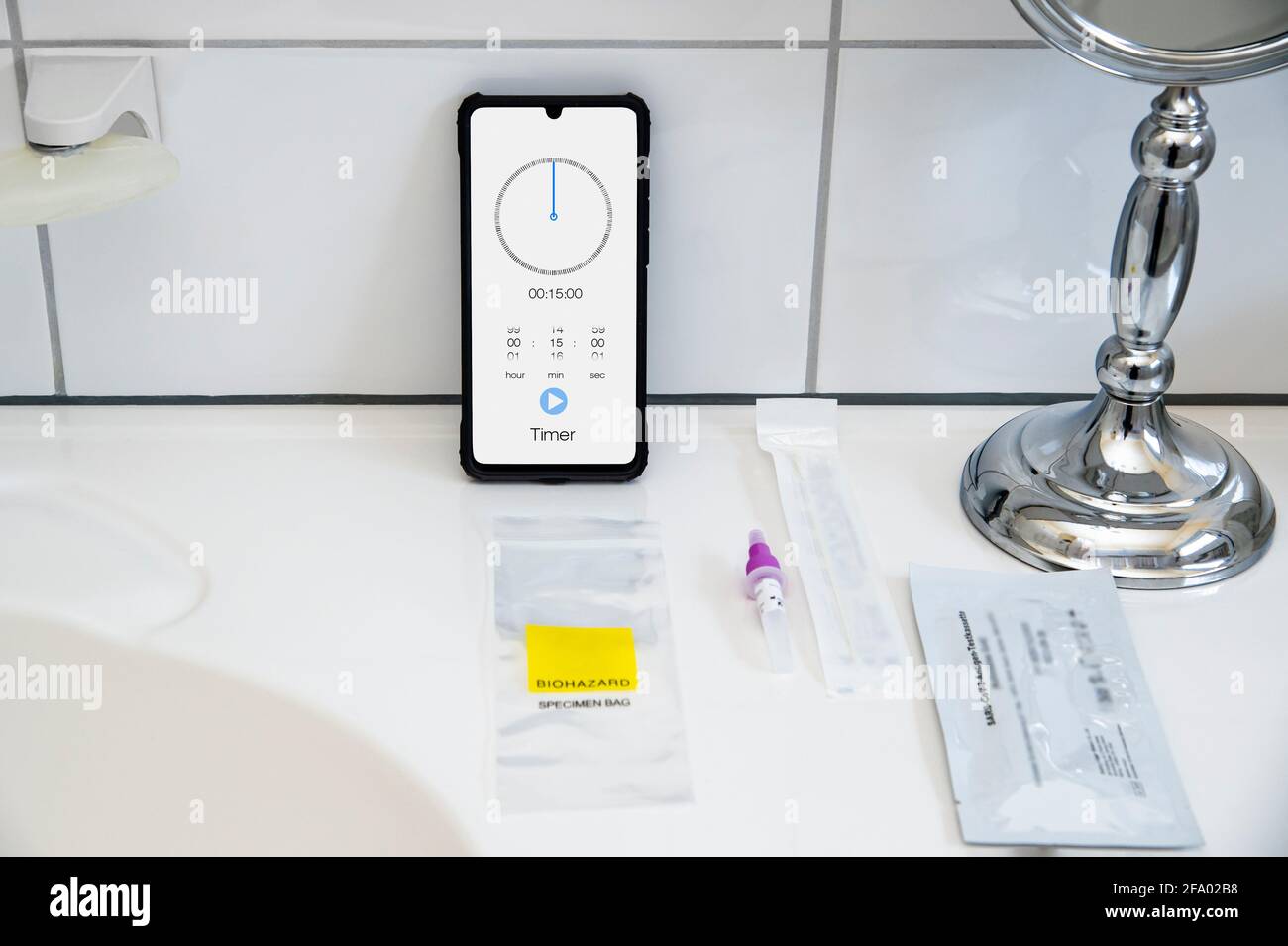 SARS CoV-2 antigen test utensils. The self test is in a bathroom on a sink. A smartphone shows how long the test has to work. German text: SARS CoV2 a Stock Photo