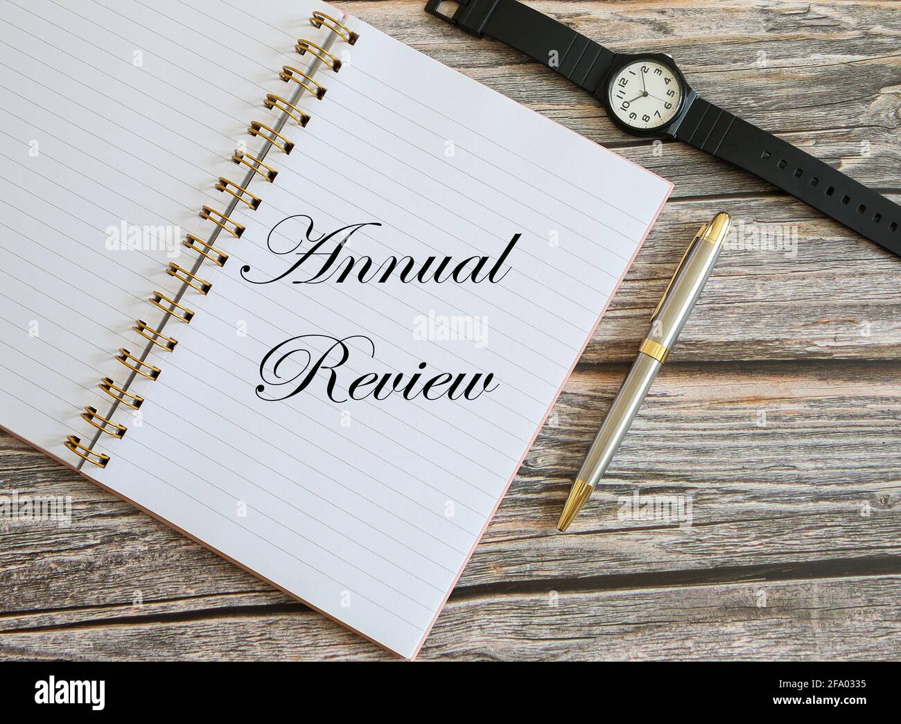 Top view of notebook, pen and watch on wooden background with a text Annual Review written in the notebook. Business and financial concept Stock Photo