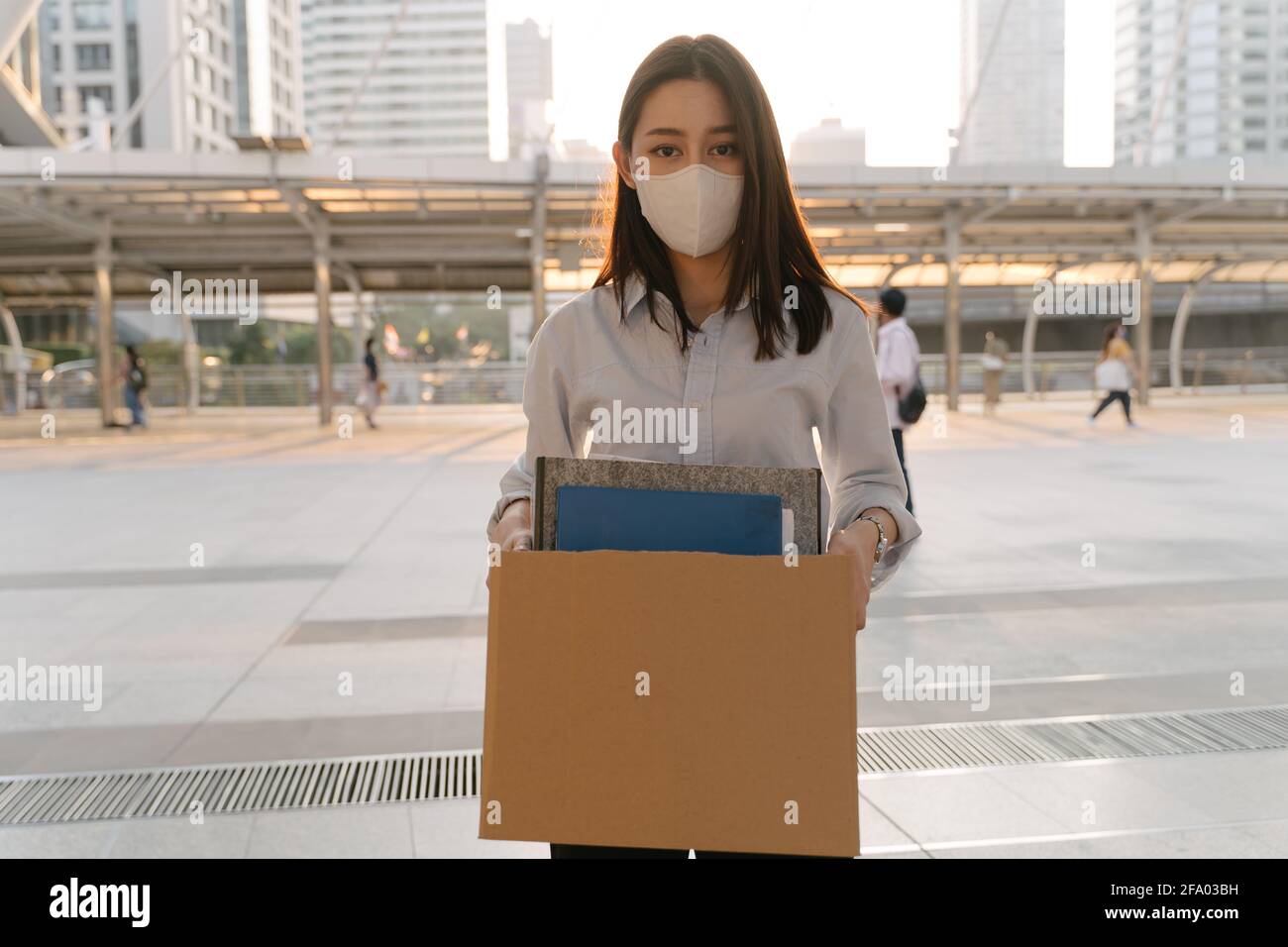 Portrait of young Asian woman wearing covid-19 protective face mask holding box of items after being laid off from job due to coronavirus Stock Photo