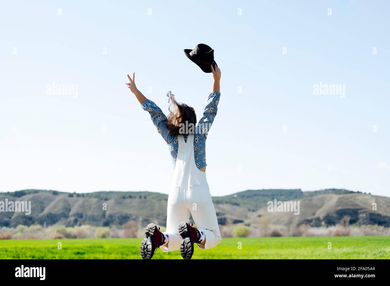 happy jumping woman in the field with hat in hand Stock Photo