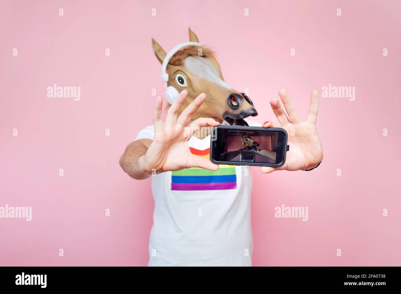man wearing horse mask while taking selfie from smartphone in studio