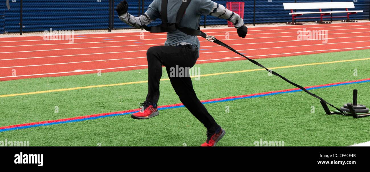 A high school track runner is pulling a sled with weights along a turf field on a cool day. Stock Photo