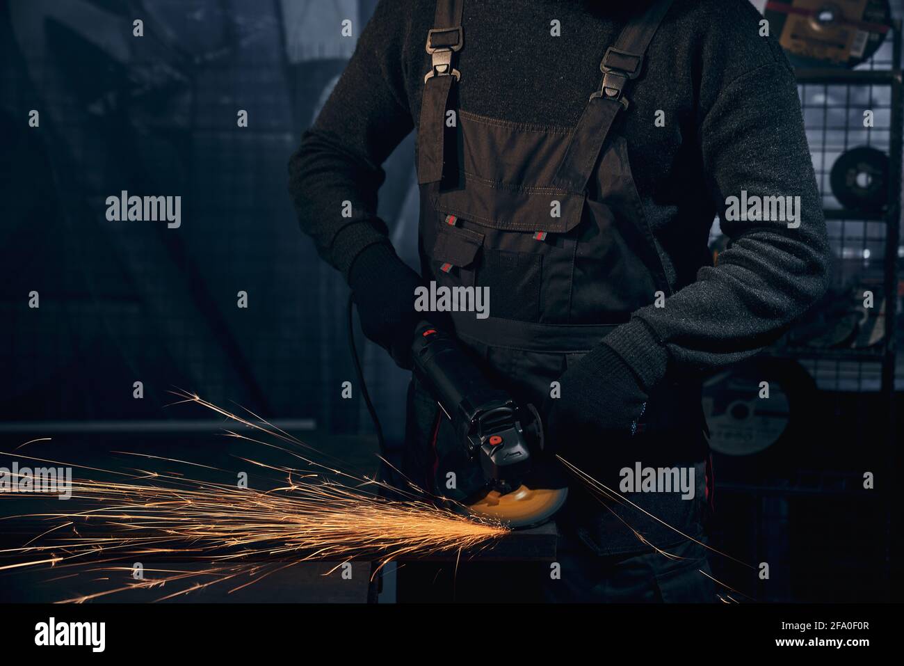 Close up of worker in special black suit and gloves working with special equipment for metal. Concept of man polishing metal in dark room or garage with angle grinder. Stock Photo
