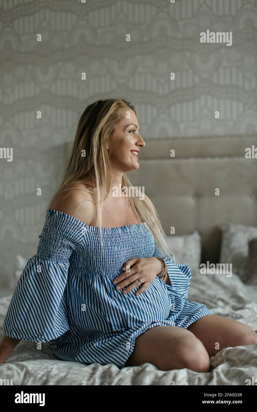 A pregnant woman resting at home and touching her belly. A happy mother to be sitting on a bed