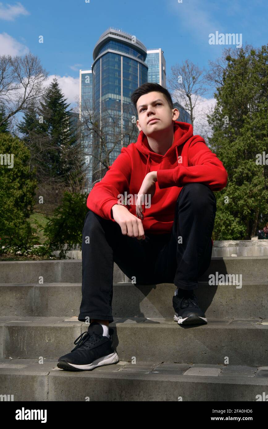 Handsome confident teenage boy sitting on the stairs in the city park on  spring sunny day. Relaxed teenager dressed red hoodie and black jeans Stock  Photo - Alamy