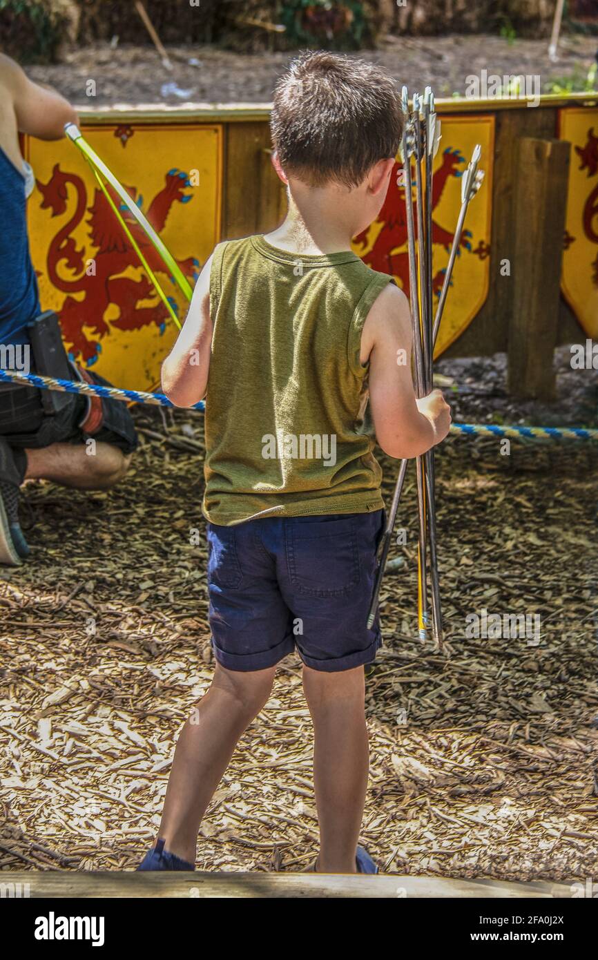Cute Little boy in shorts at outdoor shooting range with bow and arrows