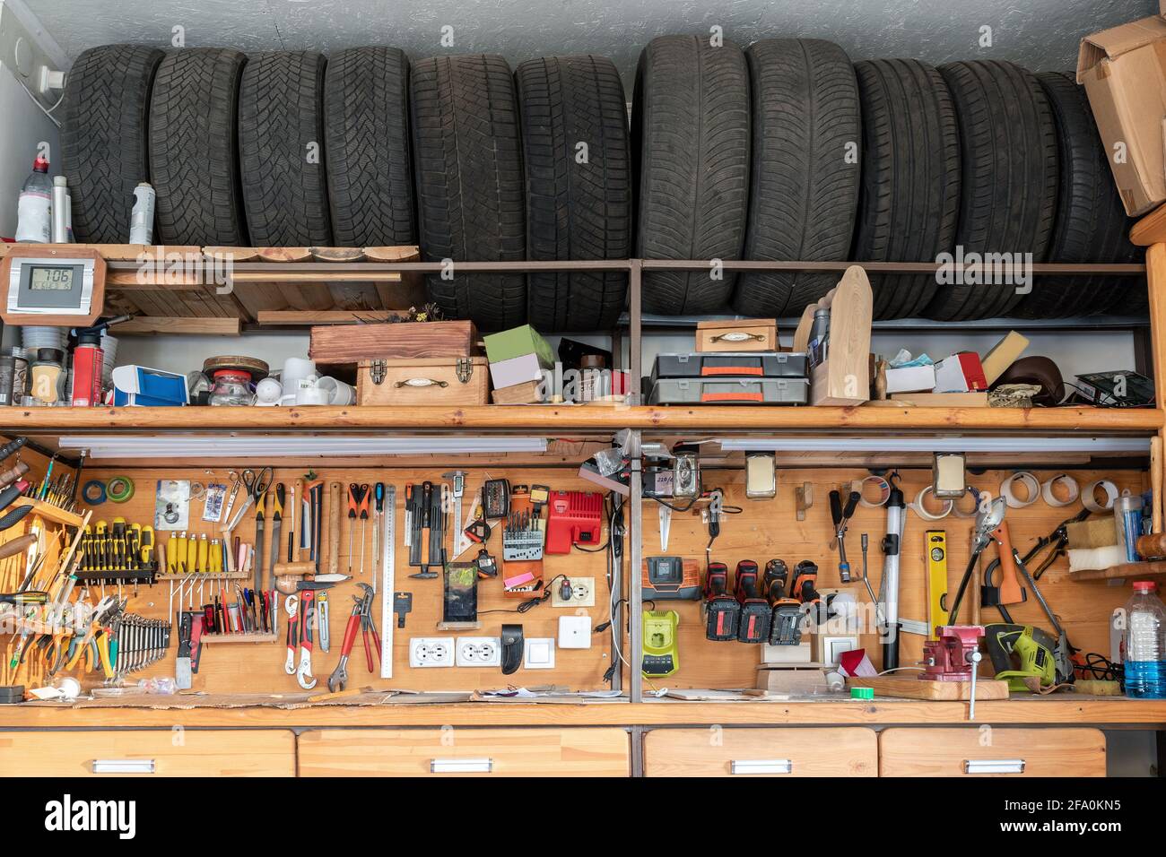 Home suburban garage interior big wooden workbench with lot of power mechanic tools at background. Spare season wheels storage shelf rack ceiling Stock Photo