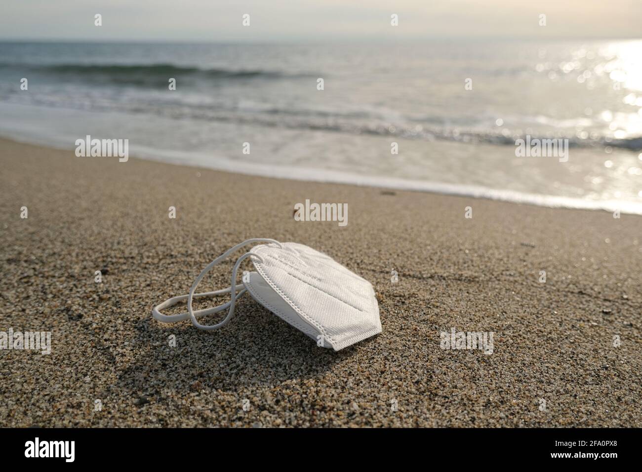 Discarded disposable face mask floating on dirty sea shore,covid19 pandemic pollution Stock Photo