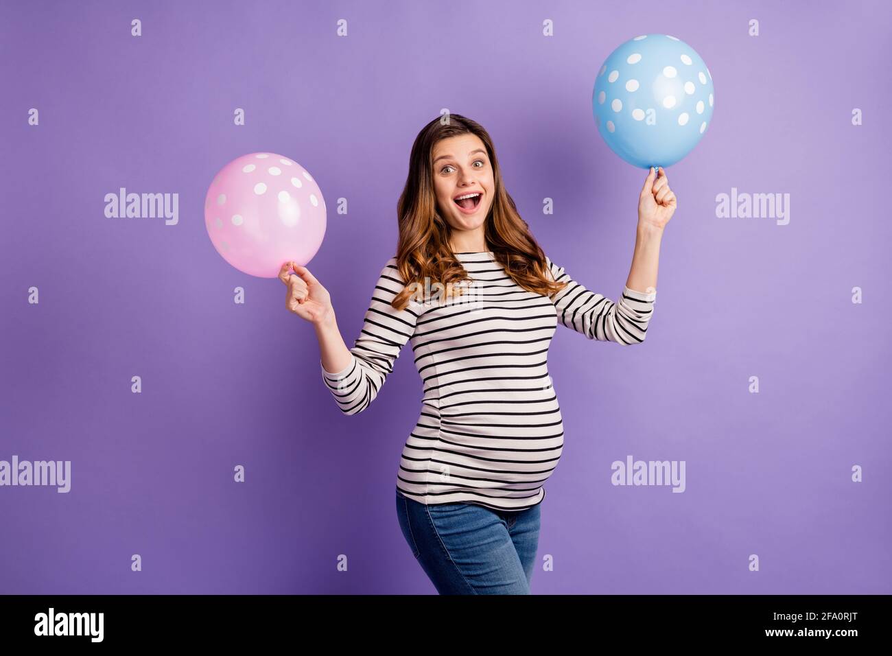 Photo portrait of pregnant excited girl holding pink and blue balloons isolated on vivid violet colored background Stock Photo