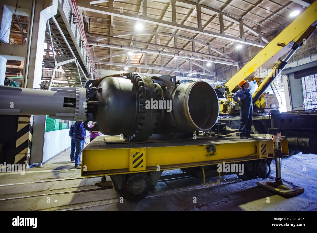 Worker lifts giant shut-off valve by mobile crane.Loading on rail platform.Oil and gas industry equipment production plant workshop.Ust-Kamenogorsk,KZ. Stock Photo
