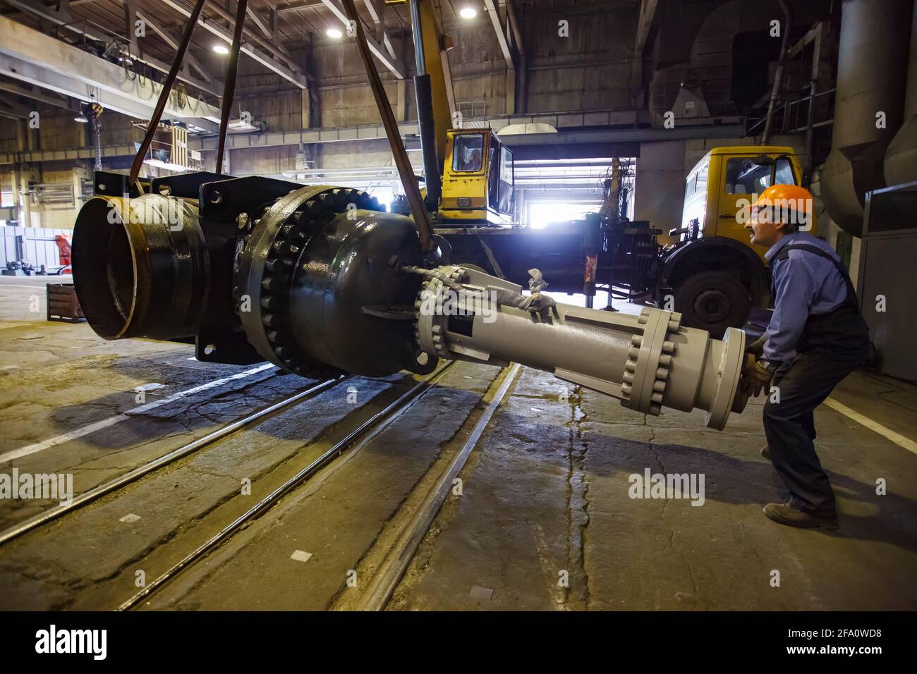 Worker lifts giant shut-off valve by mobile crane.Oil and gas industry equipment production plant workshop.Ust-Kamenogorsk, Kazakhstan. Stock Photo
