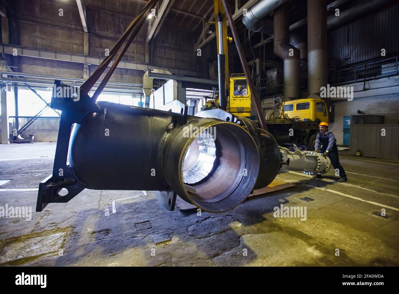 Worker lifts giant shut-off valve by mobile crane. Oil and gas industry equipment production plant workshop.Ust-Kamenogorsk, Kazakhstan. Stock Photo