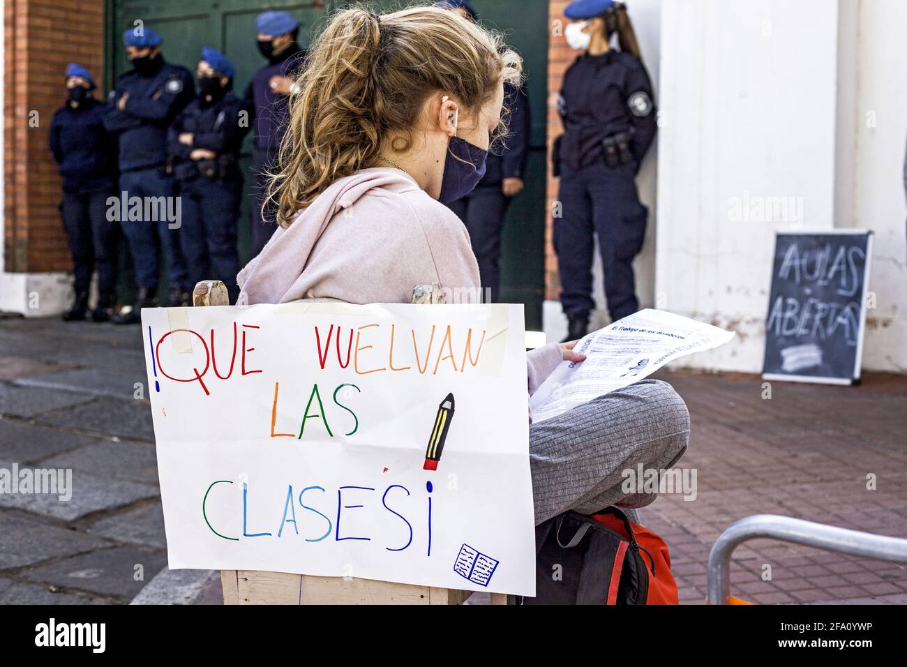 Buenos Aires, Federal Capital, Argentina. 21st Apr, 2021. A girl sits in front of police officers doing her homework outdoors in the vicinity of the Presidential Residence. On her back she carries a banner that reads: ''Que vuelvan las clases'' (Let the classes return). With Argentine schools closed, a group of parents organized a class in front of the Presidential Residence in protest against the suspension of classroom attendance for 15 days, a measure that President Alberto Fernandez ordered last Wednesday through a Decree of Necessity and Urgency to contain the resurgence of Covid-19 in t Stock Photo