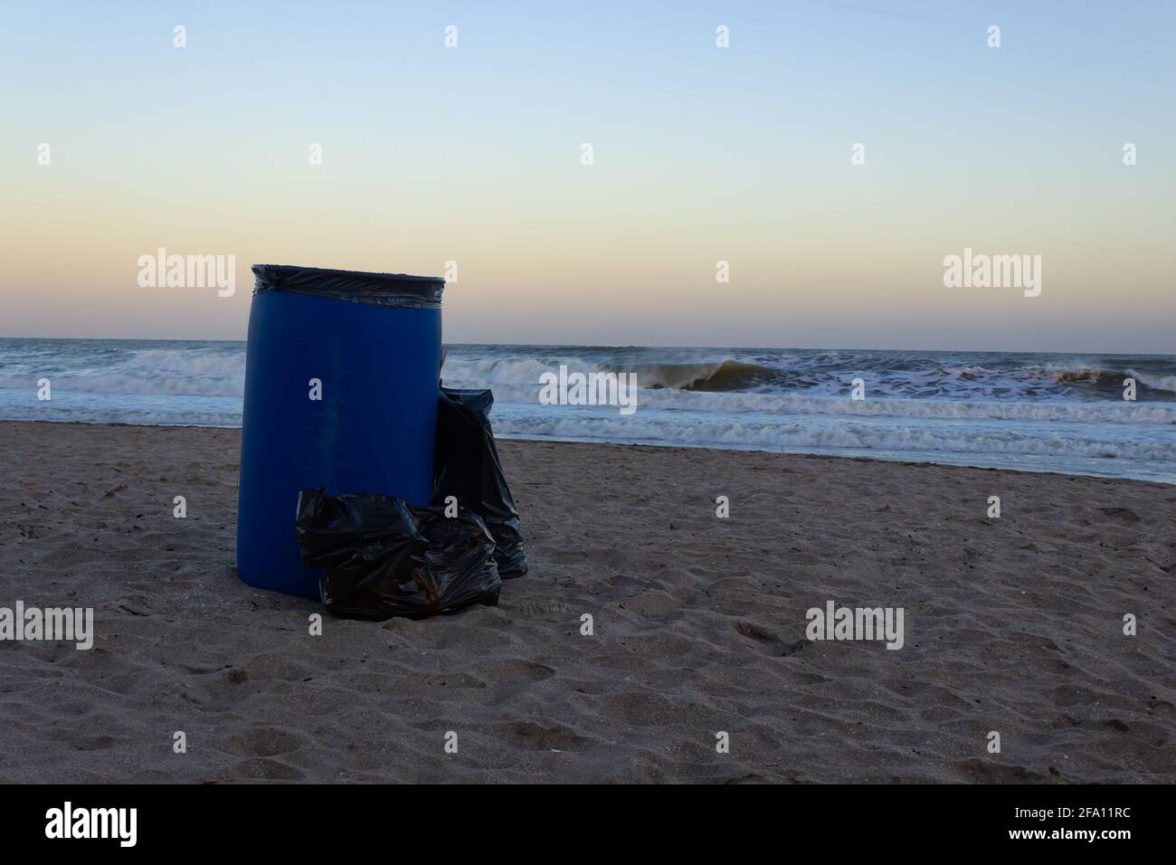 Trash can on the sand at sunrise. Stock Photo