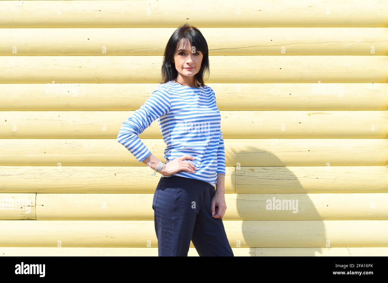 45 y.o. Russian woman standing against wooden yellow wall and looking