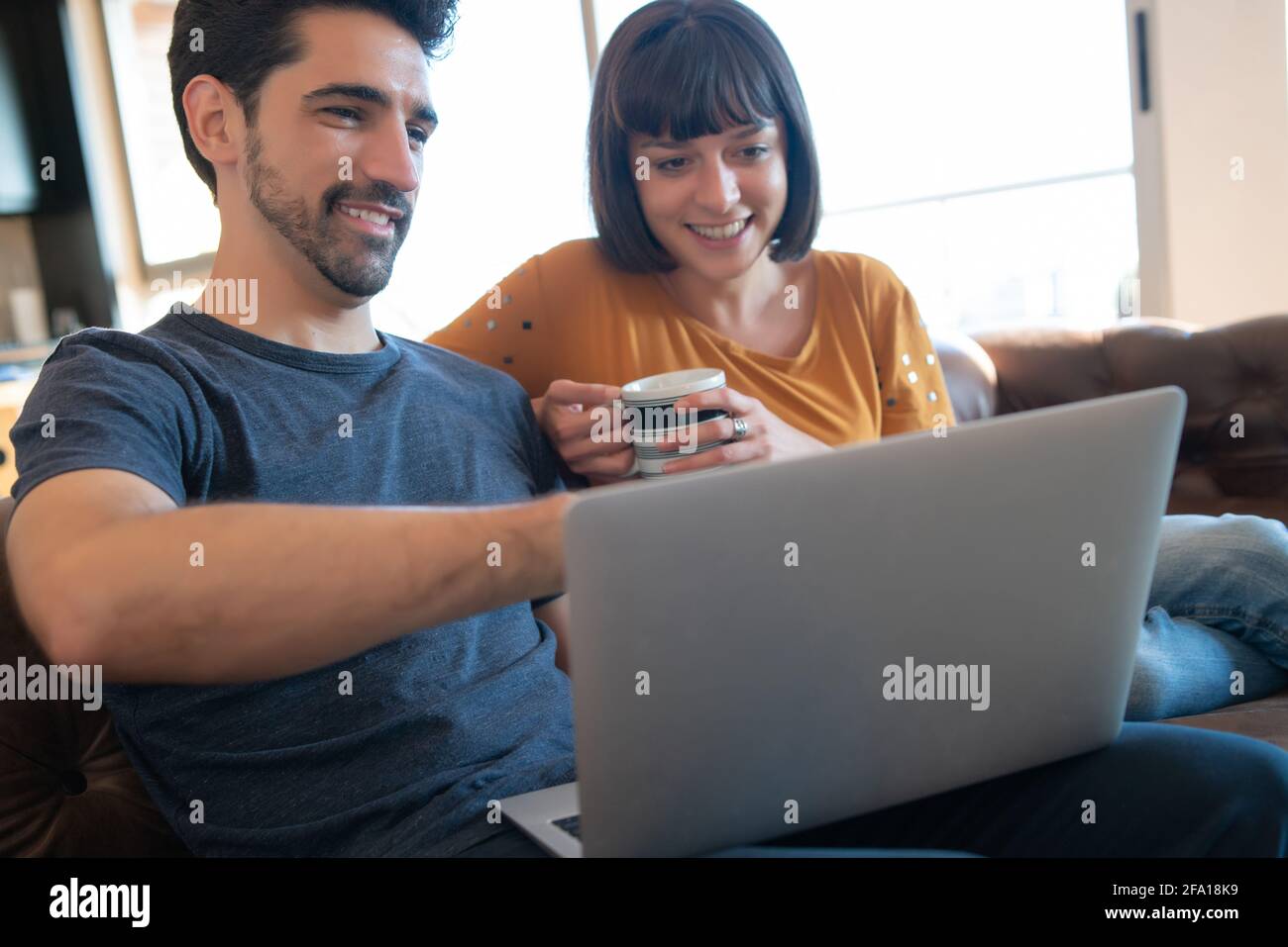 Couple using laptop while sitting on couch at home Stock Photo - Alamy