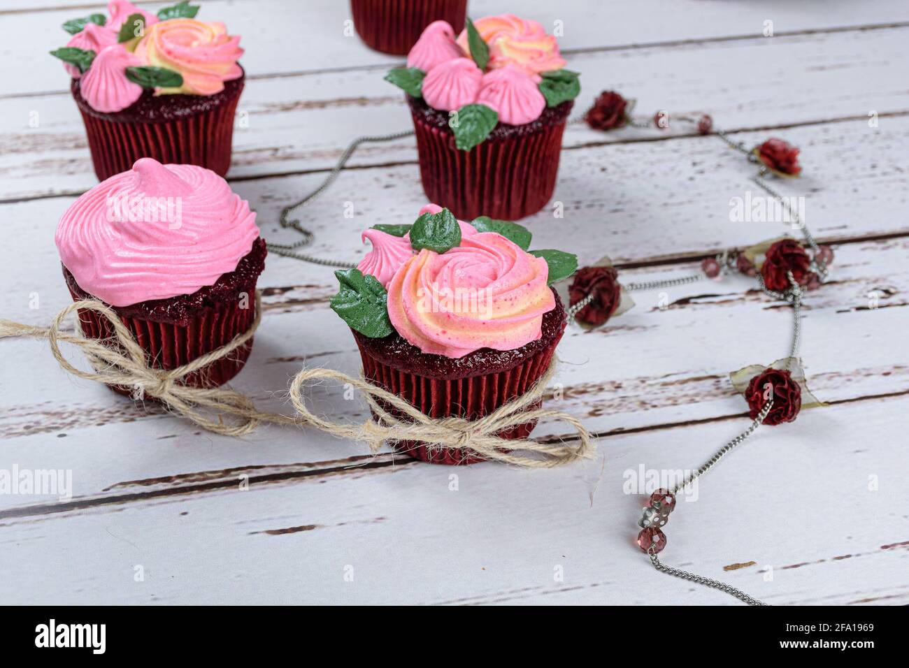 Closeup of red velvet cupcakes decorated with sisal thread bow, next to a female necklace with small roses. Stock Photo