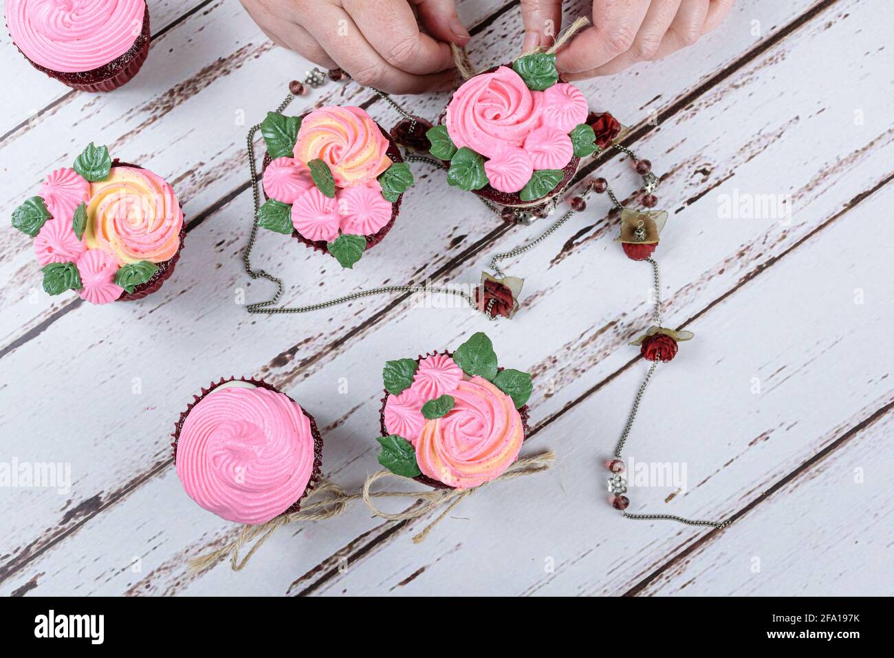 Red velvet cupcakes decorated with sisal lace, surrounded by a female necklace. Confectioner decorating a cupcake (top view). Stock Photo