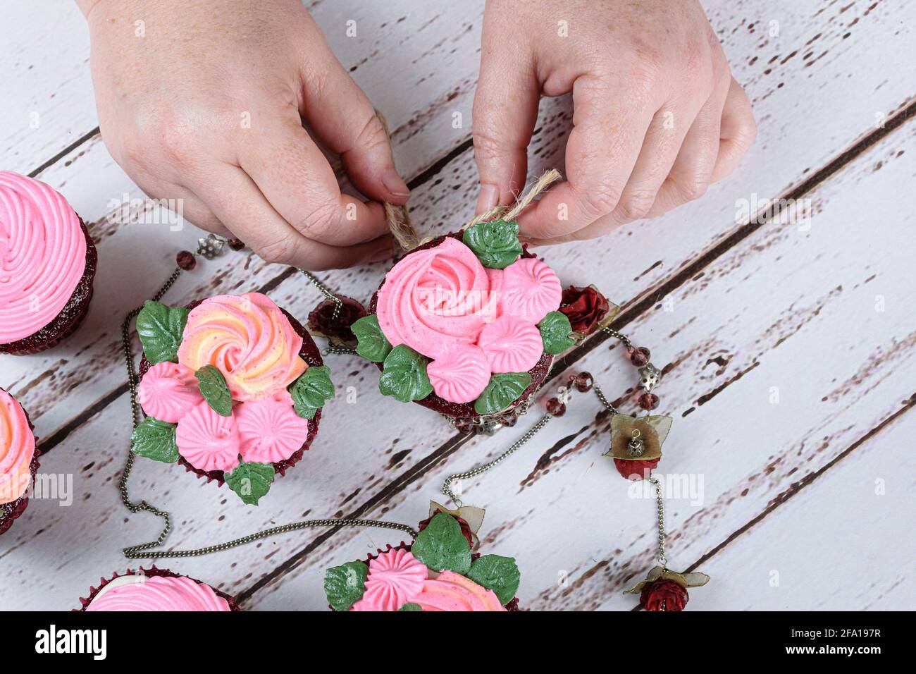 Red velvet cupcakes decorated with sisal lace, surrounded by a female necklace. Confectioner decorating a cupcake. Stock Photo