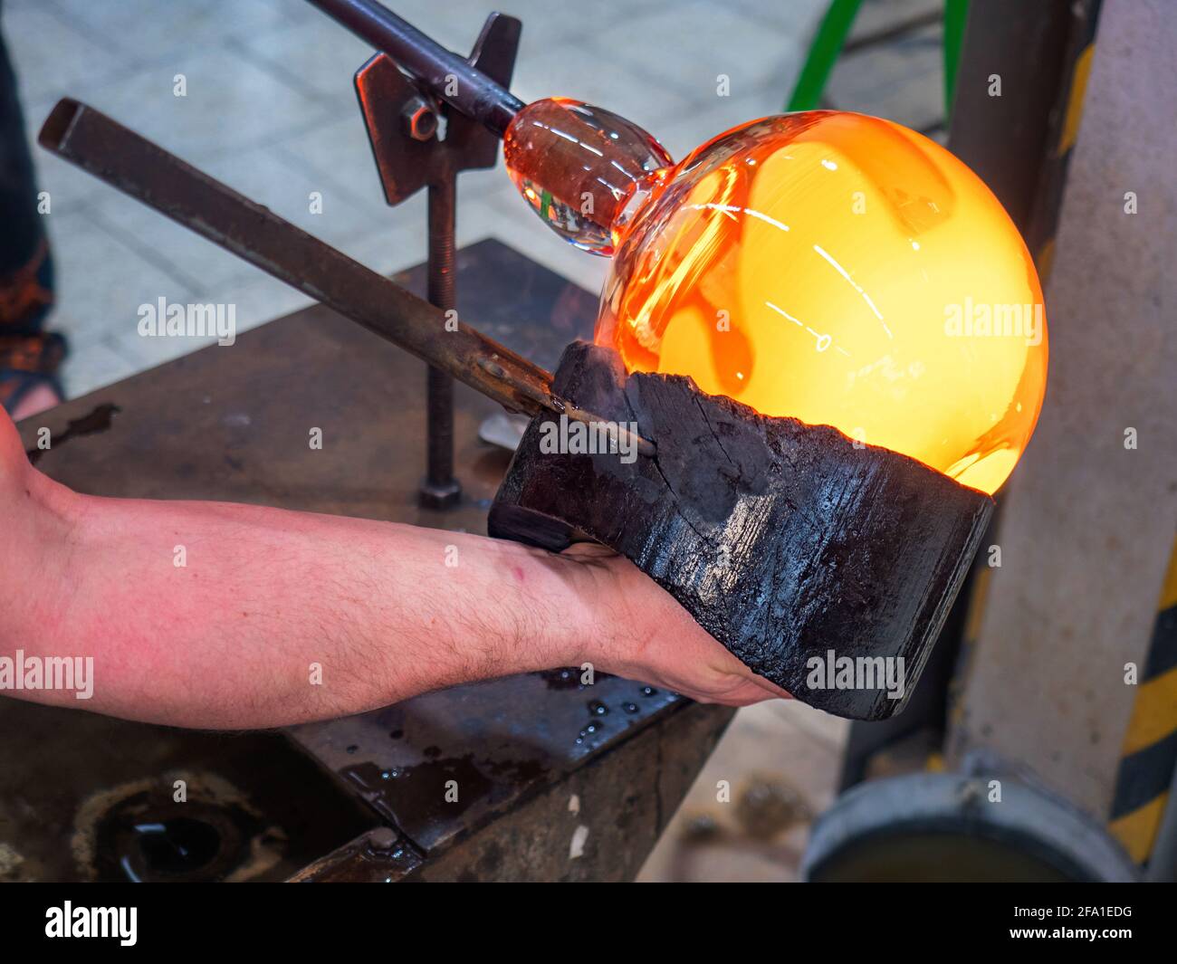 Glassblower is using wet wooden form for shaping the red melted glass