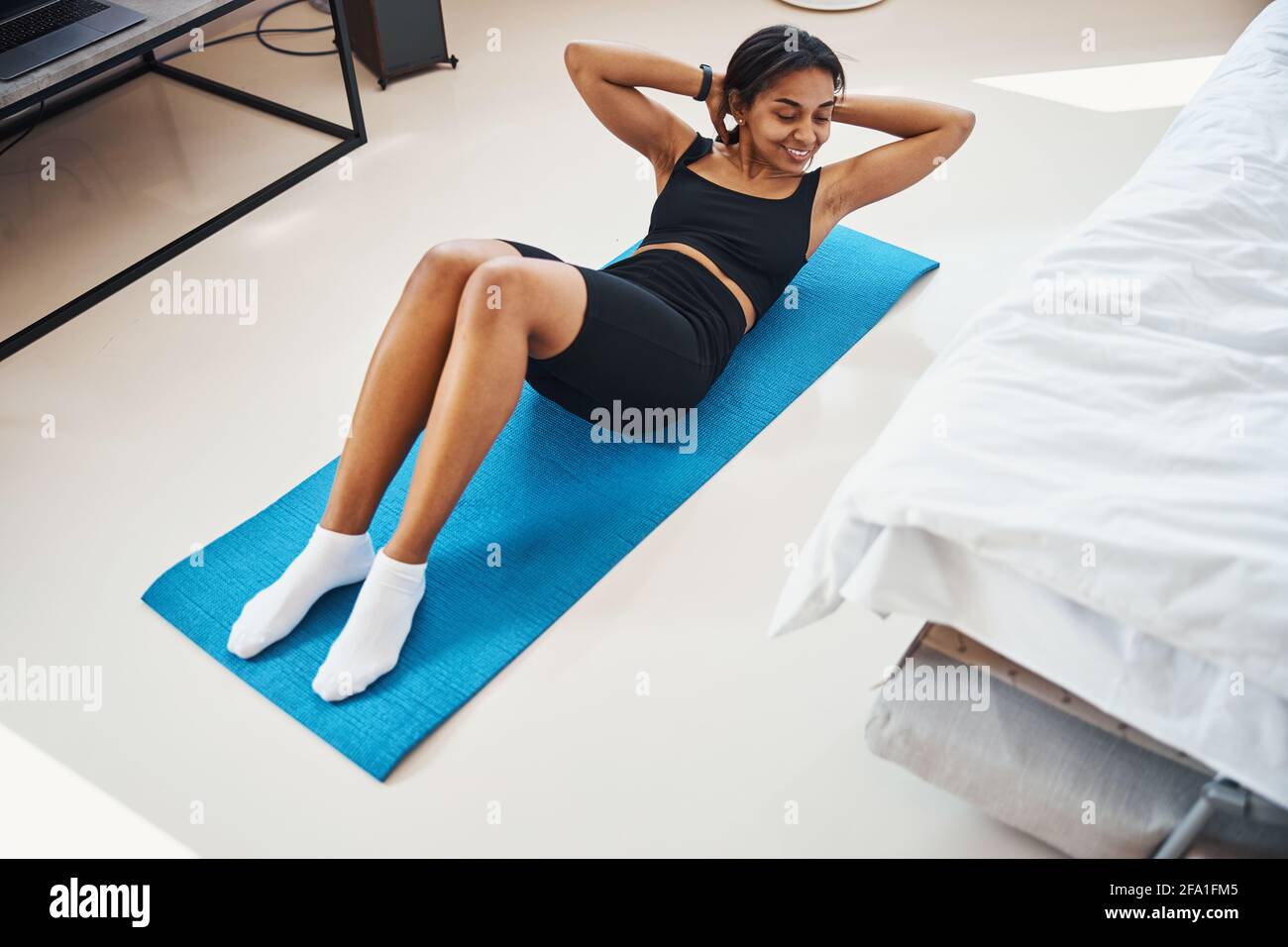 Cheerful young woman doing exercise for abs at home Stock Photo