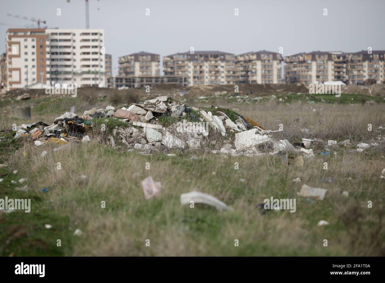 Bucharest, Romania - April 2, 2021: Piles of industrial and home waste lay on a field near inhabited blovks of flats. Stock Photo
