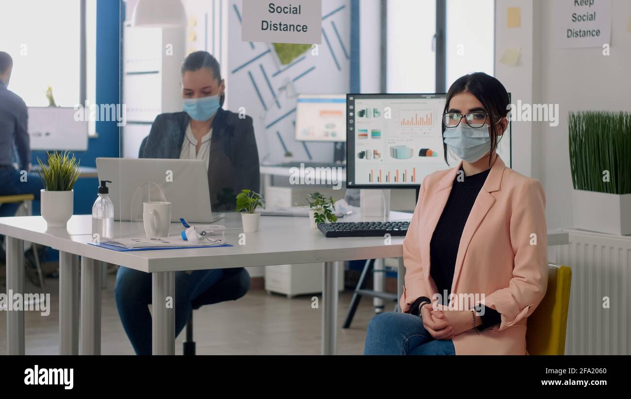 Portrait of manager with face mask sitting on chair at desk table in ...