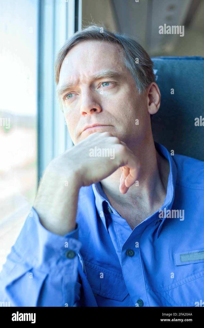 Caucasian man with serious thoughtful expression on train, looking out window Stock Photo