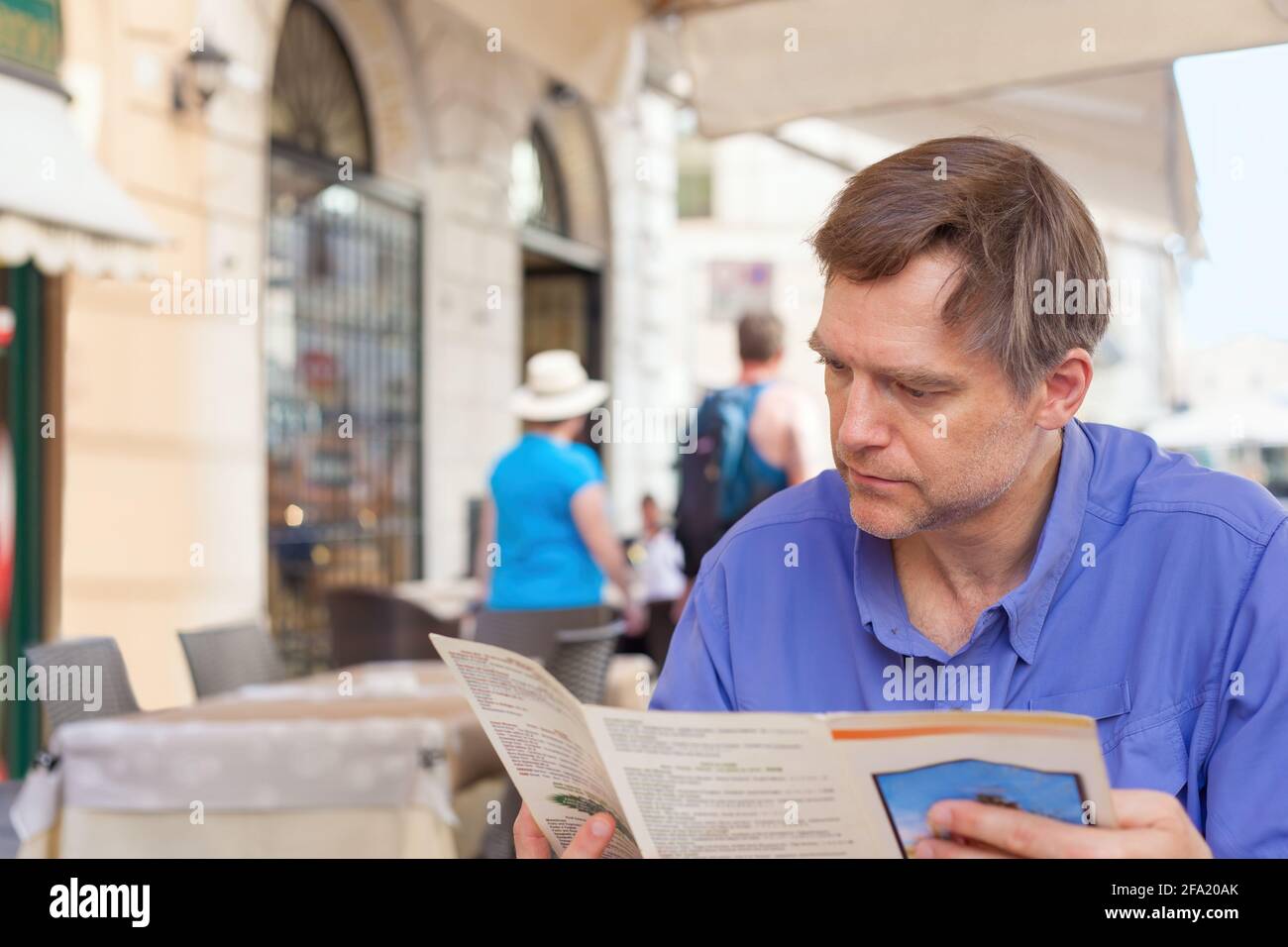 Caucasian European male tourist looking at menu of outdoor dining Italian restaurant Stock Photo