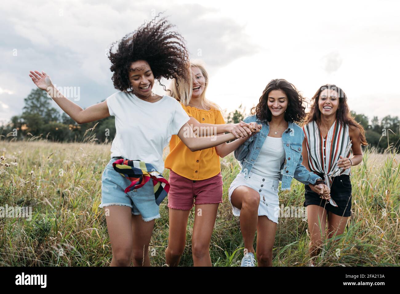 Four happy women hold hands and running on a field. Female friends having good times outdoors. Stock Photo