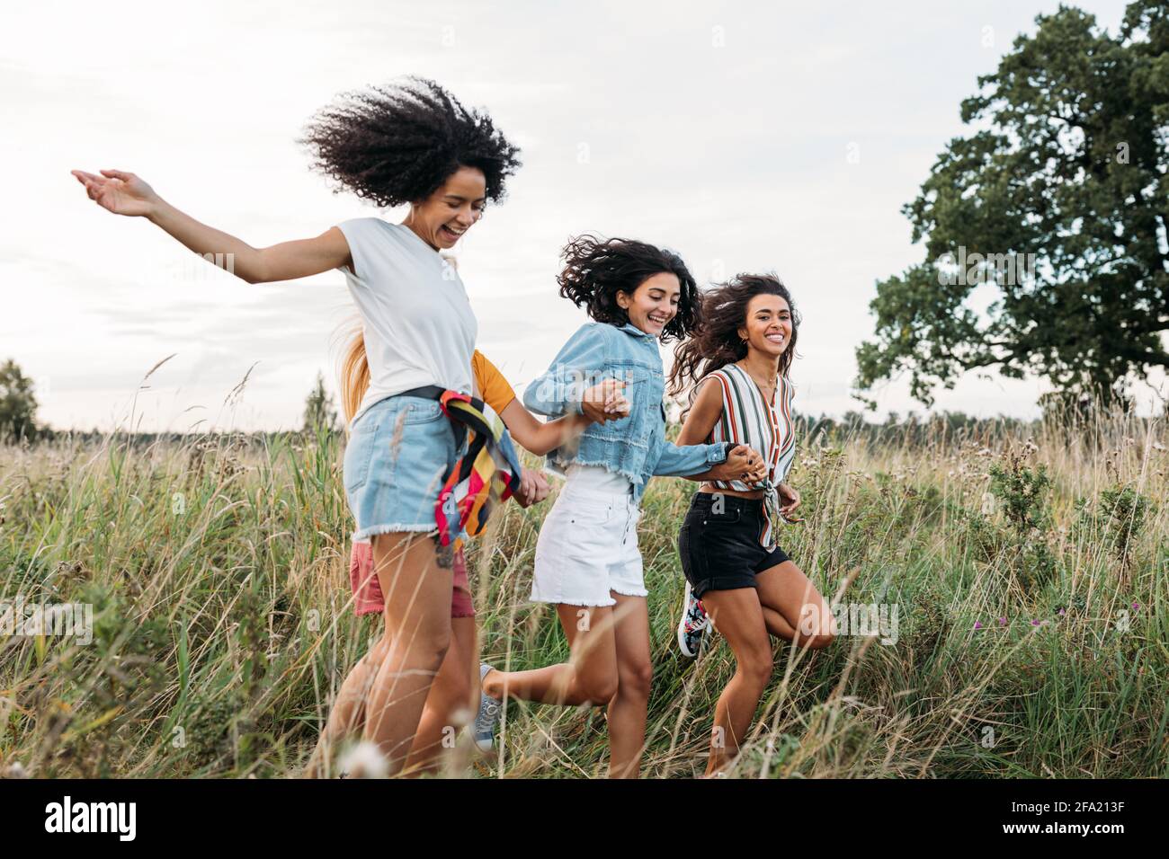 Four women holding hands running on field. Laughing friends having fun