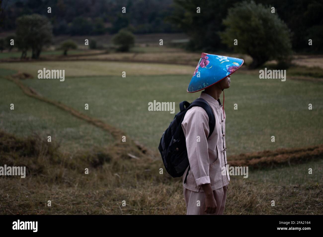 A burmese man in traditional clothing and a colorful blue hat trekking from Kalaw to Inle Lake, Shan state, Myanmar Stock Photo