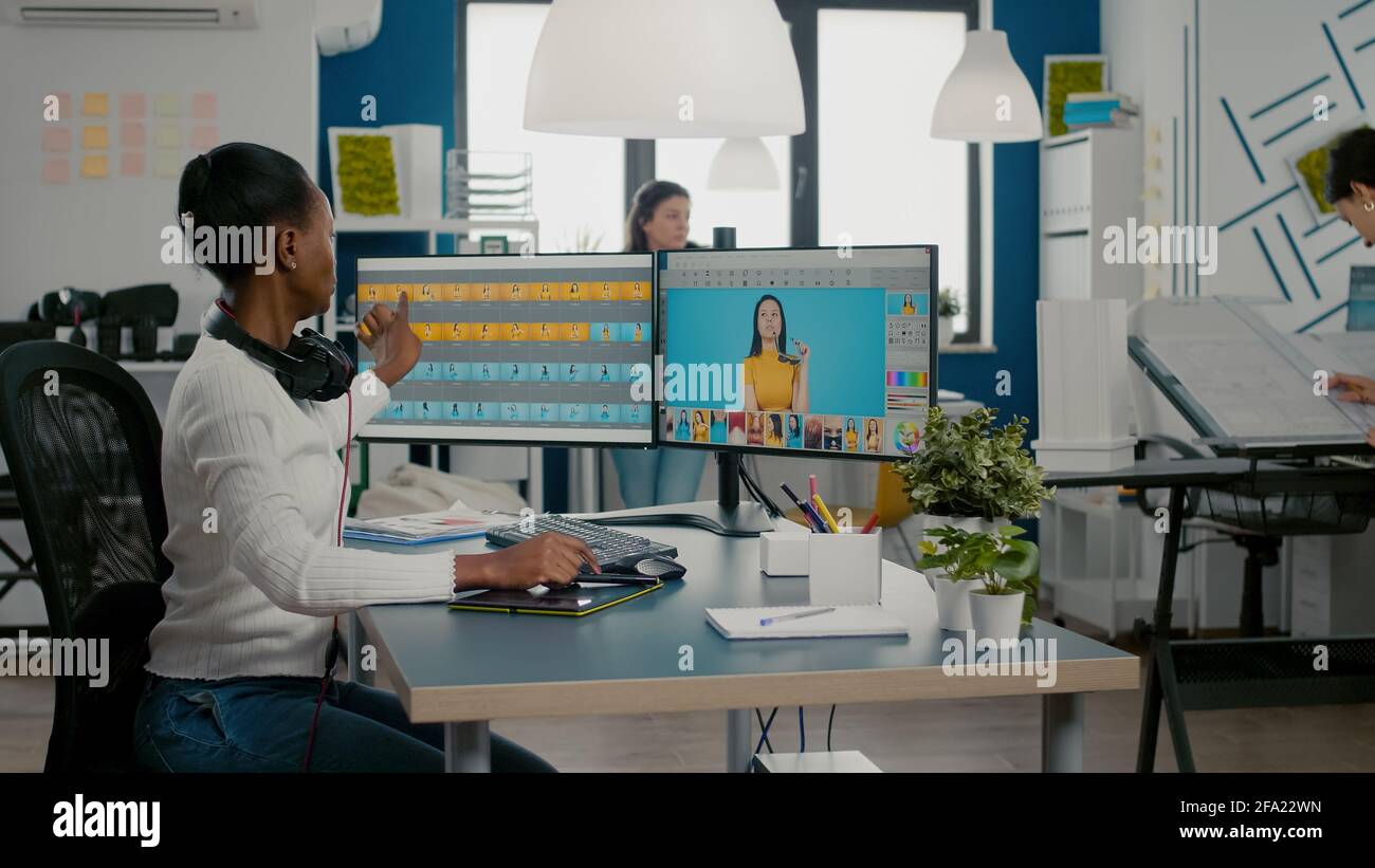 Black retoucher woman analysing images on pc with two monitors and retouching digital assets with stylus pencil. African project designer using photo editing software sitting in creative agency office Stock Photo