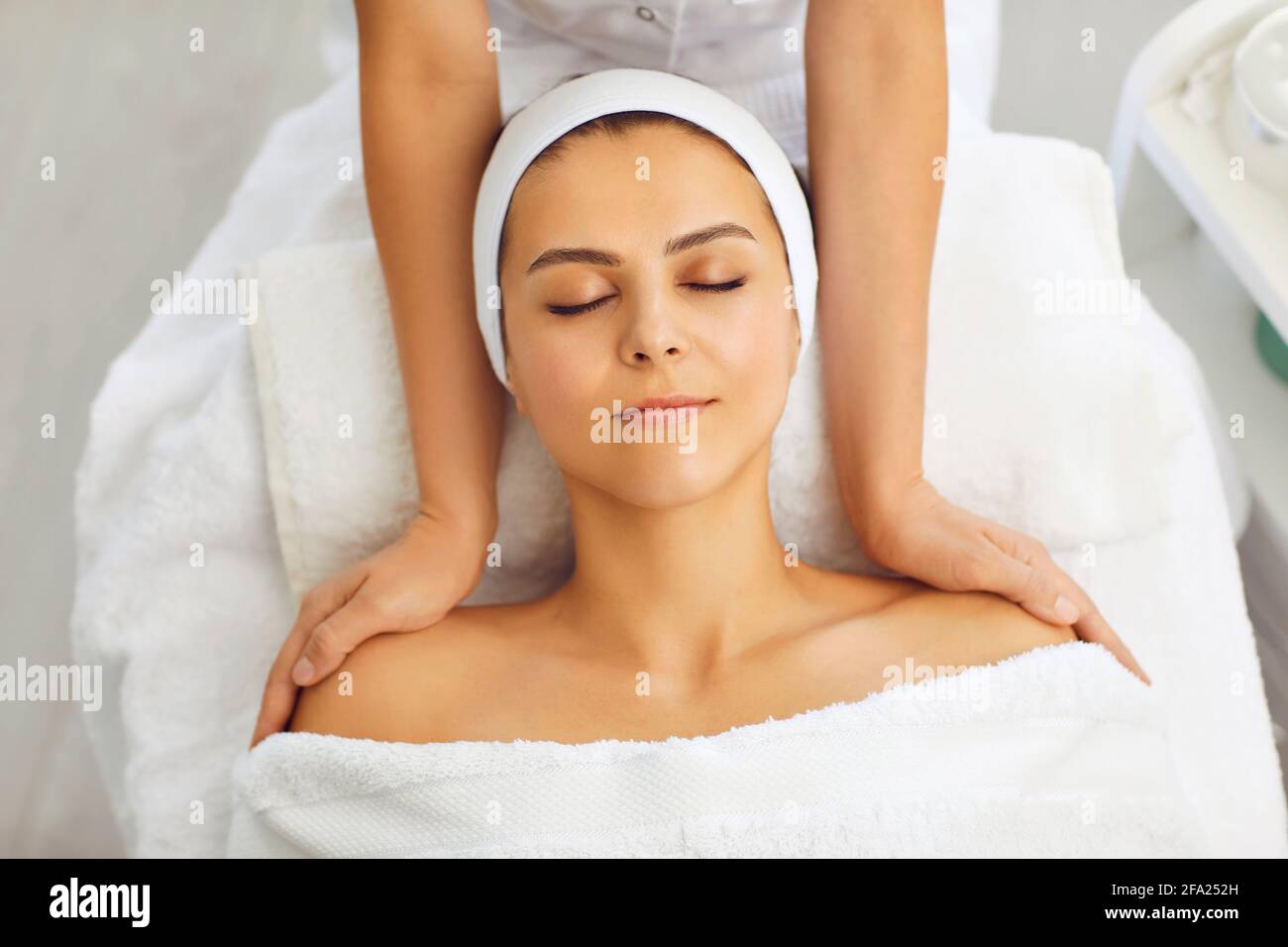 Cosmetologist making massage of face, neck and upper shoulder girdle for relaxed young woman in beauty spa salon Stock Photo