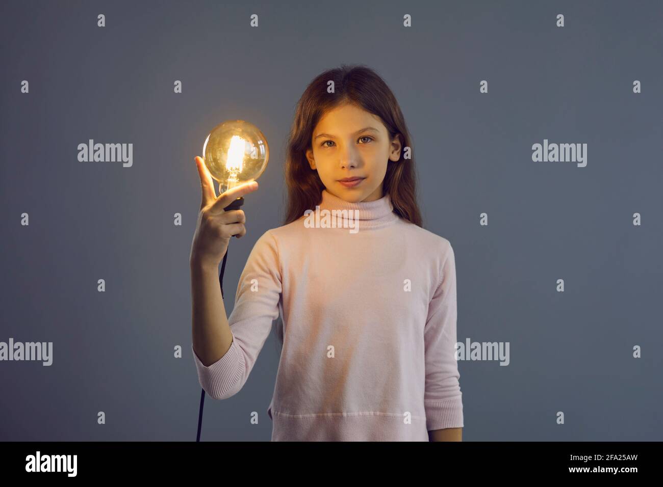 Smart intelligent pre-teen schoolgirl holding idea lamp studio shot on grey wall Stock Photo