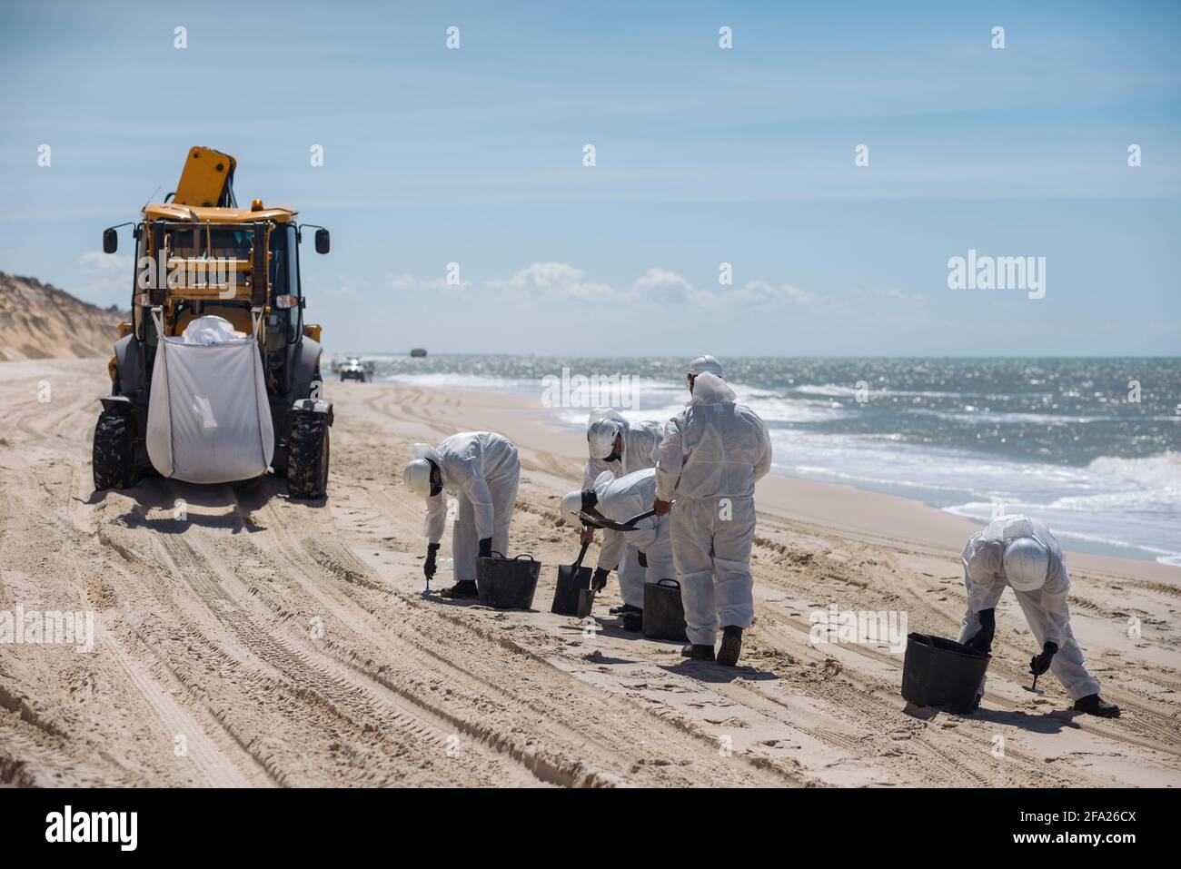 Concept: Cleaning the coast. Group of unrecognizable people with a tractor. Workers with personal protective equipment (PPE), suit, helmet and gloves. Stock Photo