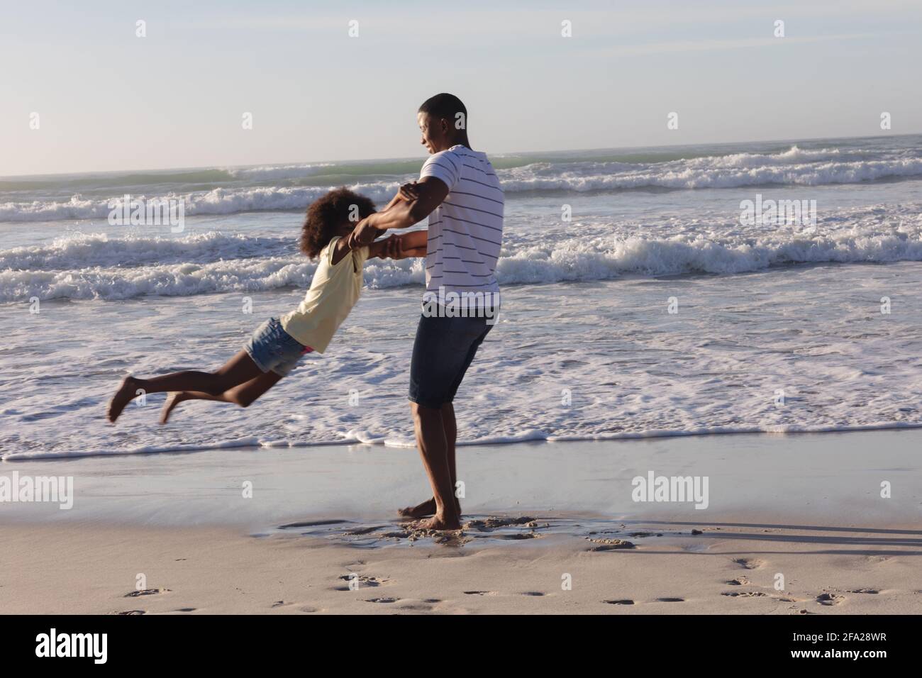 African american father and daughter having fun spinning at the beach Stock Photo
