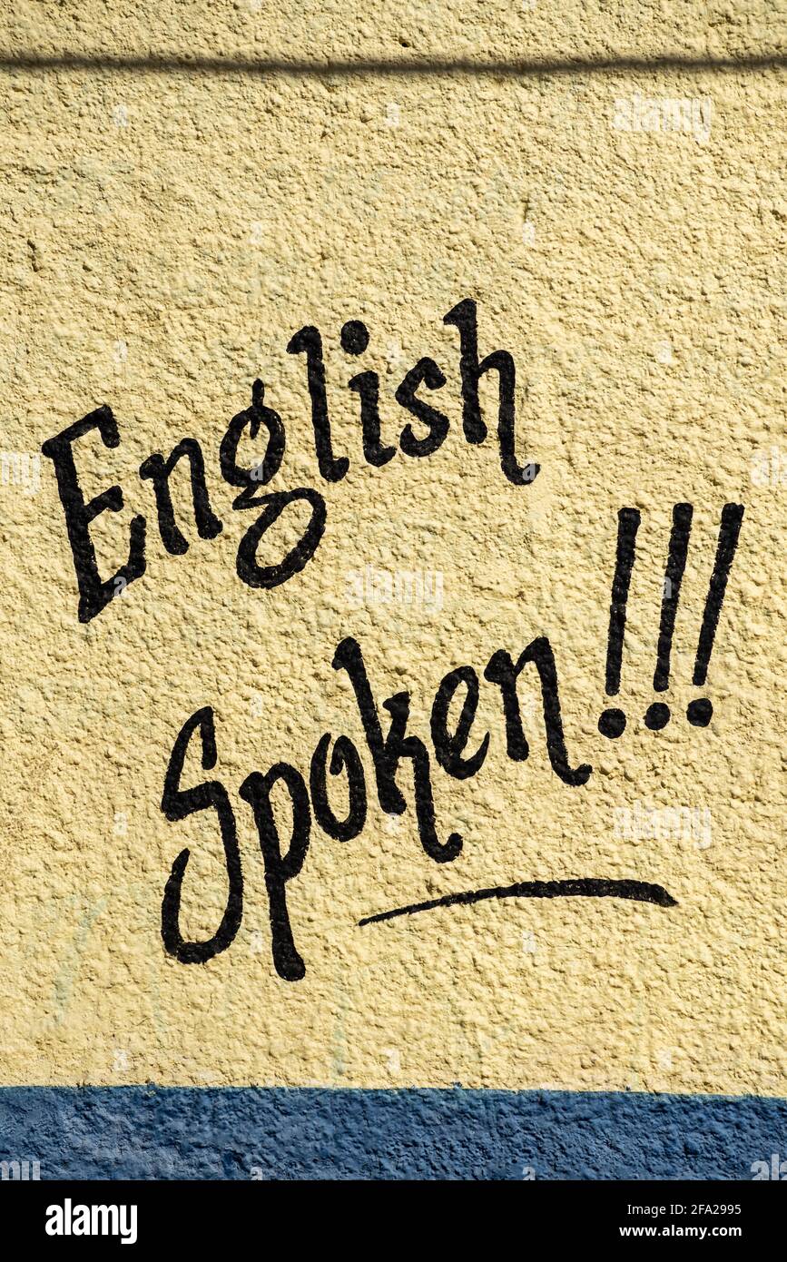 A sign hand painted on a yellow stucco wall reads English Spoken. Stock Photo