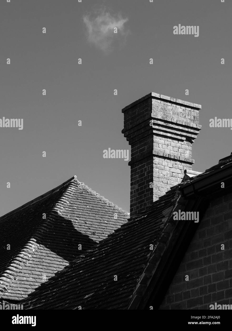 Diagonals, verticals and horizontals on a black and white image of rooflines and a chimney in Westbury, Wiltshire, England, UK., with a wispy cloud. Stock Photo