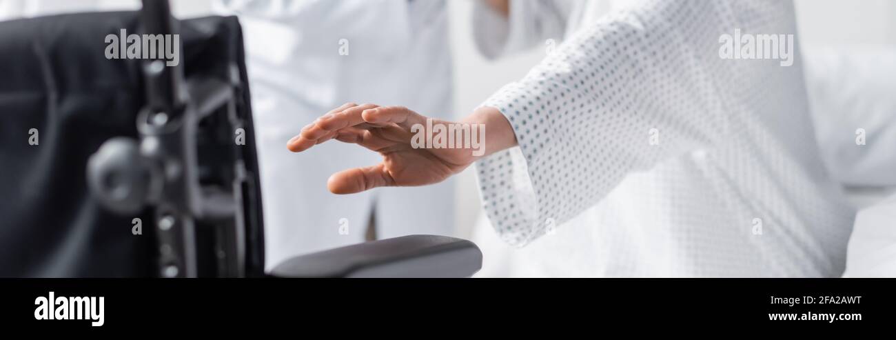 partial view of woman with outstretched hand near wheelchair on blurred foreground, banner Stock Photo