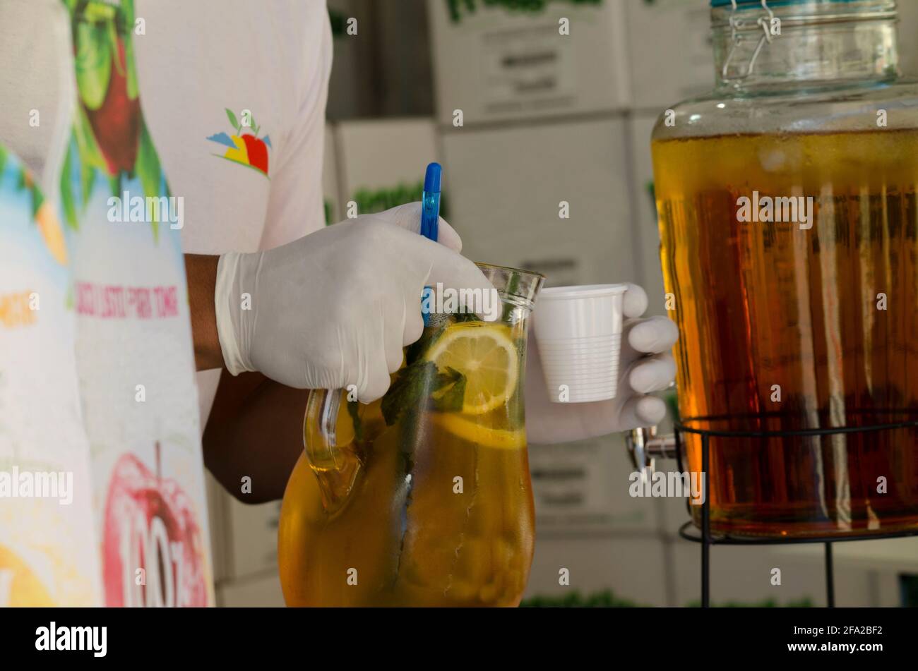 Lemon juice, lemonade or apple juice in a jug, being served by hands with latex gloves, in
