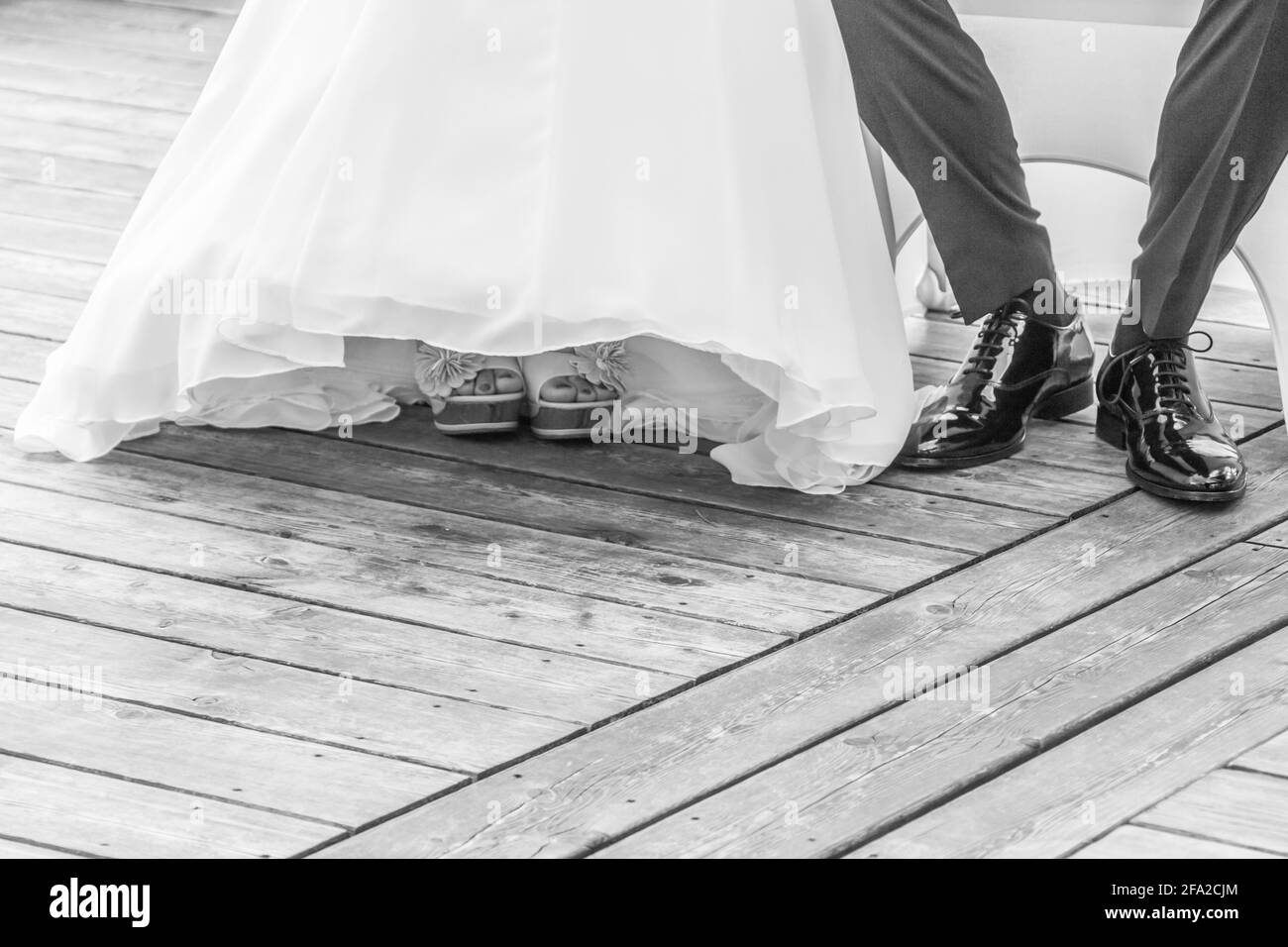 Wedding bride and groom sitting next each other at marriage. The man and the woman wearing luxury bridal dress, suit and shoes. The girl shows her fee Stock Photo