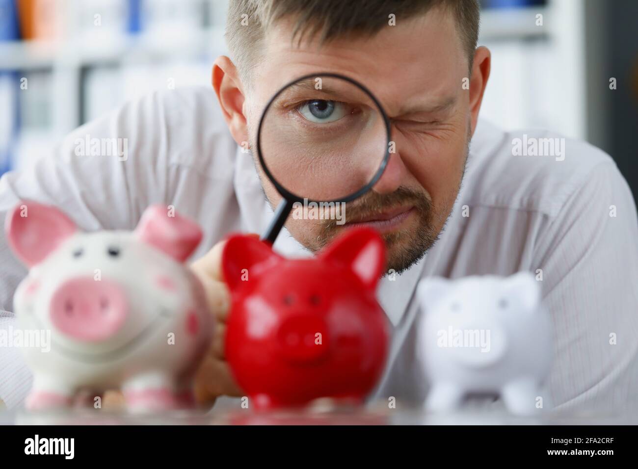 Man looks through magnifying glass at piggy bank Stock Photo - Alamy